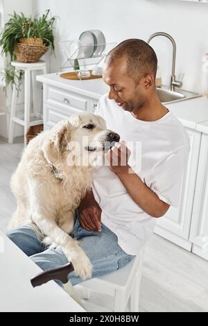 Ein behinderter afroamerikanischer Mann streichelt seinen treuen Labrador liebevoll in einer gemütlichen Küchenumgebung und strahlt Wärme und Gesellschaft aus. Stockfoto