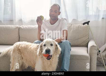 Ein behinderter Afroamerikaner sitzt auf einer Couch neben seinem treuen Labrador-Hund und zeigt Vielfalt und Inklusion. Stockfoto