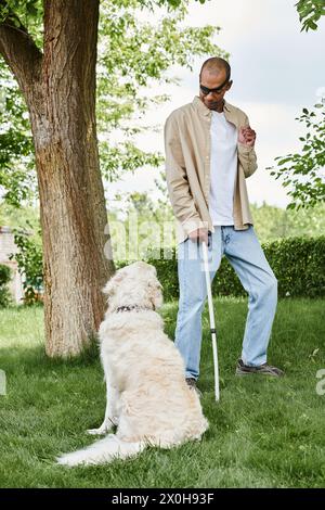 Ein behinderter Afroamerikaner mit Myasthenia gravis-Syndrom, der neben einem Labrador-Hund auf einem lebhaften grünen Feld steht. Stockfoto