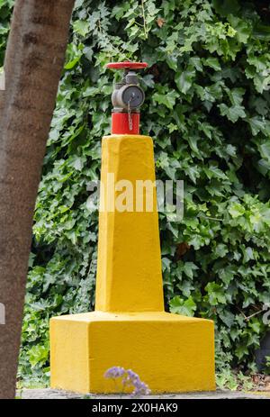 Gewährleistung des Brandschutzes, des Schutzes von Gebieten und Gebäuden vor Bränden. Ungewöhnlicher roter Hydrant an einem großen gelben Betonmast Stockfoto