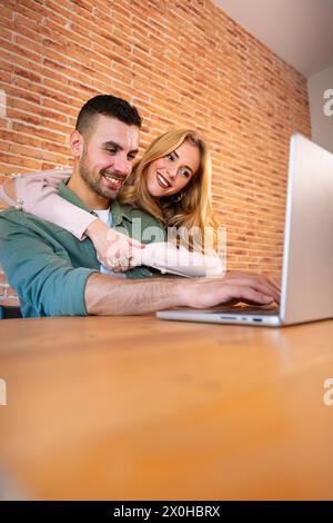 Vertikalaufnahme glücklicher Mann und Frau haben Spaß beim Surfen im Internet auf einem Laptop in Innenräumen. Stockfoto