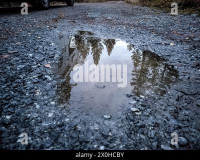 Bäume und Wohnmobil spiegeln sich in Pfützen auf Schotterwegen Stockfoto