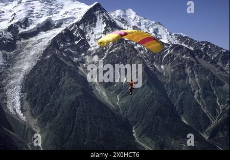 Ein von der TÃªte de Bellachat aus gestarteter Gleitschirmflieger mit gelb-rot gestreiftem Gleitschirm blickt über den Mont Blanc und den Glacier des Bossons. [Automatisierte Übersetzung] Stockfoto