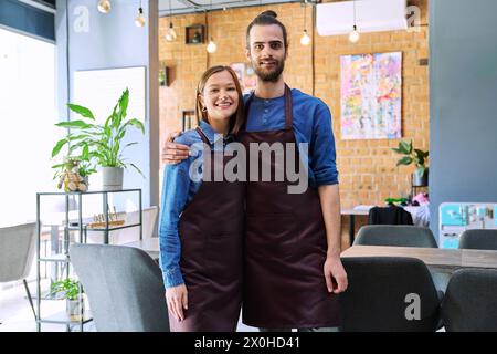 Ein paar Kollegen zu umarmen, Partner junger Mann und Frau in Schürzen am Arbeitsplatz Stockfoto