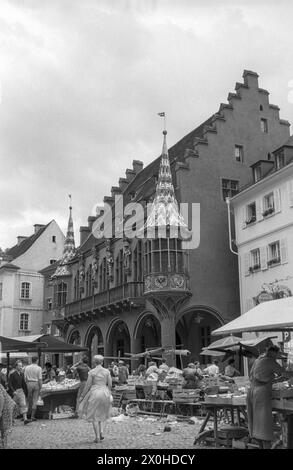 Seitenansicht des historischen Kaufhauses mit seinen Erkerfenstern. Vor ihm stehen die Marktstände auf dem Münsterplatz voller Aktivität. [Automatisierte Übersetzung] Stockfoto