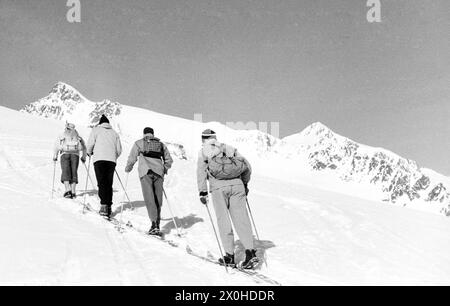 Vier Skitourenfahrer klettern einen Berg nach dem anderen auf einer einzigen Piste hinauf. [Automatisierte Übersetzung] Stockfoto