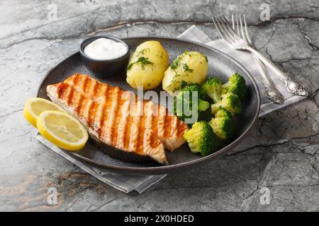 Gegrillter Lachs, gekochte Kartoffeln, Brokkoli und Sahnesauce auf einem Teller auf dem Tisch. Horizontal Stockfoto