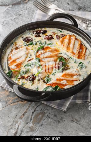 Toskanischer gegrillter Lachs in cremiger Sauce mit Spinat, sonnengetrockneten Tomaten und Parmesan in der Pfanne auf dem Tisch. Vertikal Stockfoto