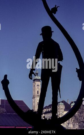 Silhouette des Karl-Valentin-Brunnens am Viktualienmarkt in München mit der Heilig-Geist-Kirche im Hintergrund. [Automatisierte Übersetzung] Stockfoto