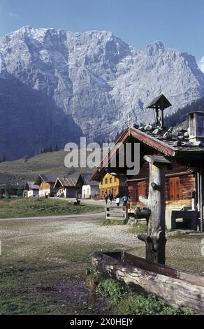 Die Almhütten mit den steilen Mauern des Karwendels. Ein Holzbrunnen davor. [Automatisierte Übersetzung] Stockfoto