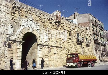 Vor der historischen Stadtmauer steht ein Tankwagen. Passanten gehen durch das Tor. Wäscherei hängt draußen auf den Balkonen zum Trocknen. [Automatisierte Übersetzung] Stockfoto