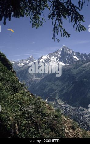 Blick auf Chamonix, Aiguille Verte und Aiguille du Dru. Ein Gleitschirmflieger mit einem rot-gelben Gleitschirmflieger am blauen Himmel. [Automatisierte Übersetzung] Stockfoto