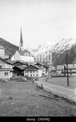 Eine schmale Straße führt zu den Häusern des Dorfes, in deren Mitte die Kirche mit ihrem Turm steht. Die Berge im Hintergrund sind teilweise mit Schnee bedeckt. [Automatisierte Übersetzung] Stockfoto