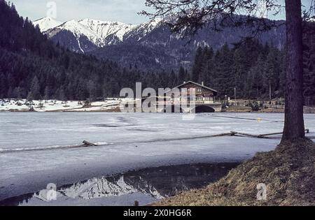 Der See ist immer noch mit Eis bedeckt, schneebedeckte Berge spiegeln sich in einem eisfreien Abschnitt wieder. [Automatisierte Übersetzung] Stockfoto