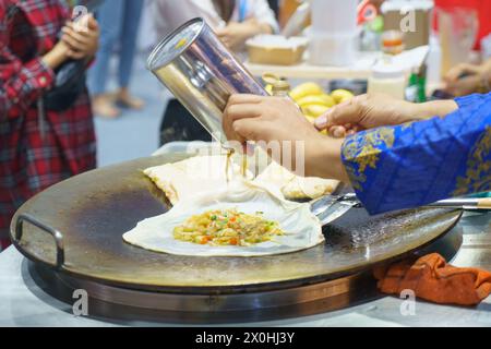 Tauchen Sie ein in die belebten Straßen Thailands mit dieser lebendigen Szene. Ein erfahrener Verkäufer bereitet auf fachmännische Weise knusprige Roti zu, ein beliebtes Street Food de Stockfoto