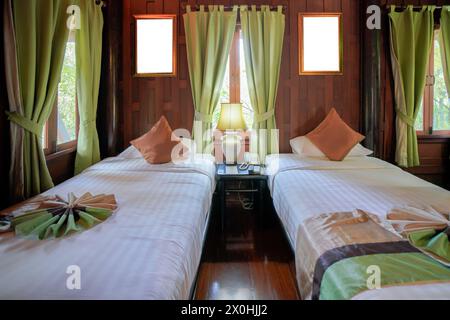 Gemütliches und intimes Zweibettzimmer mit traditionellem thailändischem Dekor, Holzwänden und Kunstwerken, gedämpfter natürlicher Beleuchtung und lebhaftem Grün Stockfoto