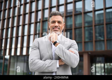 Glücklicher Geschäftsmann mittleren Alters, der einen Anzug trägt und draußen steht. Hochformat. Stockfoto