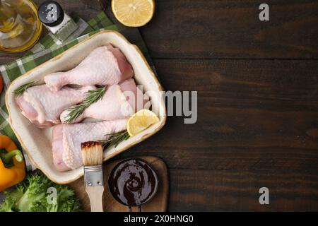 Flache Lagenkomposition mit Marinade und rohen Hähnchenkeulen auf Holztisch. Leerzeichen für Text Stockfoto