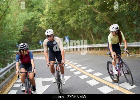 Drei junge asiatische Radfahrer, die auf der Landstraße im Freien Fahrrad fahren Stockfoto