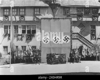 Zwei SS-Dienstposten stehen vor dem Dreibund für die Rede von Funktionären der NSDAP mit dem Adler vor dem Rathaus in Ochsenfurt anlässlich der Feierlichkeiten zum Arbeitstag am 1. Mai 1933. [Automatisierte Übersetzung] Stockfoto