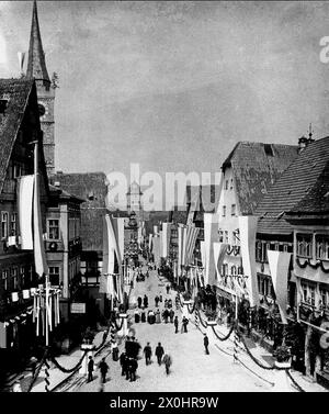 Menschen an der Hauptstraße in der Altstadt von Ochsenfurt schmückten sich anlässlich eines Festtags mit Fahnen. [Automatisierte Übersetzung] Stockfoto