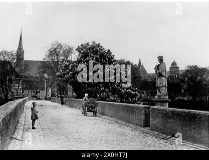 Eine alte Frau zieht einen Wagen voller Holz an einem Kind vorbei auf der Alten Mainbrücke in Ochsenfurt. [Automatisierte Übersetzung] Stockfoto