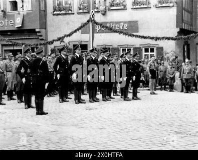 Eine Aufstellung der Schutzstaffel (SS) mit SA- und Werkstruppen im Hintergrund und daneben eine Hitlerjugend im Festzug zum Arbeitertag vor dem Rathaus in Ochsenfurt. [Automatisierte Übersetzung] Stockfoto