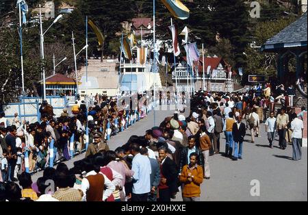 Die Zuschauer warten auf den Besuch der ehemaligen indischen Premierministerin Indira Gandhi in Shimla. Sie führen eine eng gepackte Straße. Es ist mit Flaggen dekoriert. Auf der Straße läuft ein uniformierter Mann den Gang hinunter. [Automatisierte Übersetzung] Stockfoto