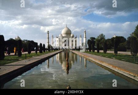 Blick auf das Taj Mahal Grab der Mumtaz Mahal in der Nähe der Metropole Agra aus dem Süden. Im Vordergrund steht ein langes Wasserbecken, ein so genannter Tschah?r B?gh, und Teile des umliegenden Gartens. In der Verlängerung der Längsachse thront das Taj Mahal unter bewölktem Himmel. [Automatisierte Übersetzung] Stockfoto