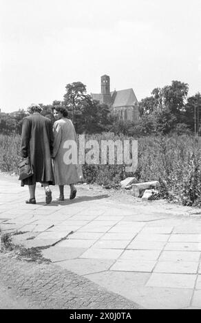 Zwei Frauen, die auf einem Bürgersteig laufen. St. Im Hintergrund ist die Adalbertkirche zu sehen, deren Turm noch keinen Spitzturm hat. [Automatisierte Übersetzung] Stockfoto