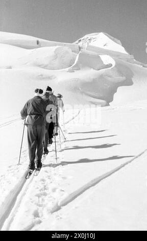 Vier Skitourenfahrer klettern einen Berg nach dem anderen auf einer einzigen Piste hinauf. [Automatisierte Übersetzung] Stockfoto