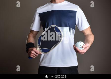Detail des Pickleball-Spielers mit Sportbekleidung und Schläger und Spielball in den Händen auf grauem isoliertem Hintergrund. Stockfoto
