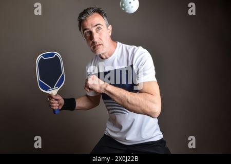 Detail eines professionellen Pickleball-Spielers, der einen weißen Ball auf einem isolierten grauen Hintergrund trifft. Stockfoto