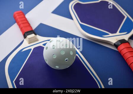 Blaue und rote Pickleball-Paddel aus Holz und ein weißer Ball auf blauem Spielplatz. Erhöhte Aussicht. Stockfoto