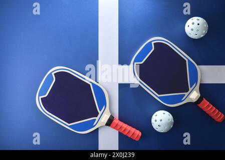 Blaue und rote Pickleball-Paddel aus Holz und weiße Kugeln auf blauem Spielplatz. Draufsicht. Stockfoto