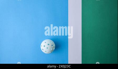 Hintergrund mit weißer Pickleball-Kugel auf einer blau-grünen Spielfläche mit weißer Linie. Draufsicht. Stockfoto