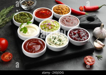 Verschiedene leckere Saucen in Schüsseln und Zutaten auf grauem Tisch Stockfoto
