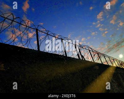 Betonzaun mit Metallbarben auf blauem Himmel Hintergrund. Sichere Umrandung mit Stacheldraht. Technische Schutzwand für den Außenbereich. Verbotene Industrie Stockfoto