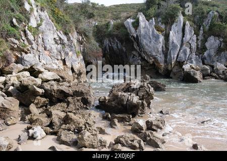 Ein felsiger Strand in Llanes, Asturien, mit einem von großen Felsen umschlossenen Gewässer. Der Strand ist zerklüftet und natürlich, das Wasser liegt sanft auf einem Stockfoto