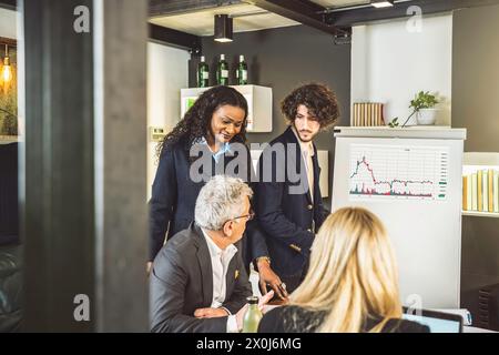 Das Team aus verschiedenen Teams analysiert Markttrends in einem Diagramm. Multikulturelle und generationenübergreifende Gruppe, die sich mit Focus und prof an strategischen Geschäftsgesprächen beteiligt Stockfoto