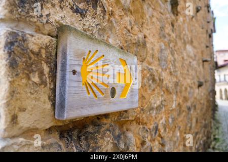 An der Seite eines robusten Steingebäudes befindet sich ein Schild, das die Wegbeschreibung für den Jakobsweg in Spanien anzeigt. Die verwitterte Str. Stockfoto