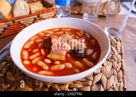 Eine Schüssel mit Fabada Asturiana, einer traditionellen spanischen Bohnen- und Fleischsuppe, steht auf einem Holztisch. Die Suppe ist herzhaft und geschmackvoll, enthält Te Stockfoto