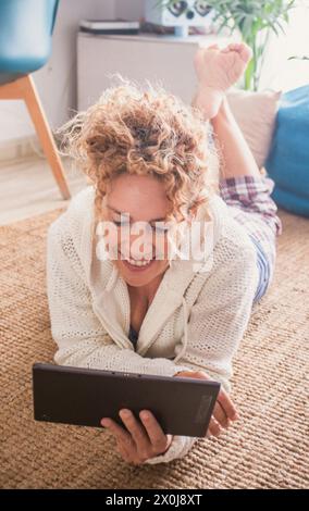 Frau, die zu Hause auf dem Teppichboden liegt und Laptop-Gerät mit Internetverbindung benutzt. Weibliche Leute, die surfen und die Kommunikation genießen. Eine Person mit Technologie Stockfoto