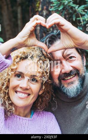 Glückliches erwachsenes Paar verliebte Menschen machen Herdsymbol-Geste mit Händen zusammen lächelnd und genießen die Beziehung. Mann und Frau Freizeit mit grünem Laubwald im Hintergrund. Stockfoto