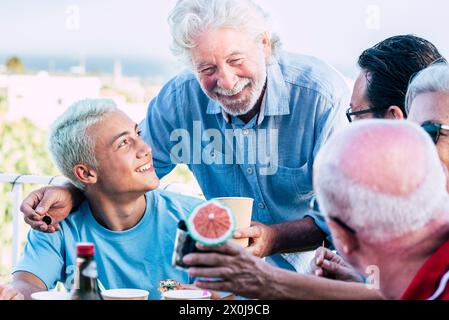 Gemischte Generationen Familien genießen gemeinsam Essen und feiern im Freien. Junge Teenager und Großväter haben Spaß zusammen in Freundschaft, essen und trinken vom Tisch Stockfoto