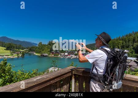 Tourist mit schwarzem Hut und Rucksack fotografiert mit Smartphone, Blick von Malerwinkel Seterrasse zum Königssee, Bootsanlegestelle, im Hintergrund Unterbergmassiv mit Hochthron, 1972 m, und Almbach Wand, Schönau am Königssee, Berchtesgadener Land, Bayern, Deutschland, Europa Stockfoto