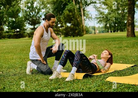 Eine Frau Sportswear auf einer gelben Matte im Freien, geführt von ihrem Personal Trainer in einer Yoga-Sitzung voller Entschlossenheit und Motivation. Stockfoto