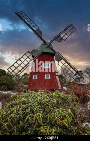 Typische historische Windmühle aus rotem Holz in einer Winterlandschaft. Das Gebäude liegt auf einem Felsen an der Küste. Abend in Stenungsund, Schweden Stockfoto