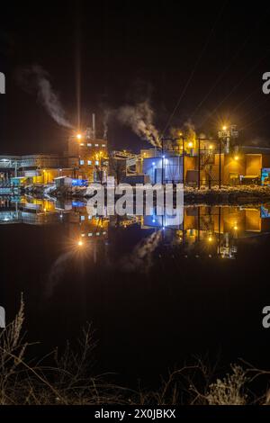 Papierfabrik in der Nacht. Winterfoto einer kleinen Fabrik mit Reflexion in einem See. Nachtszene in Bengtsfors, Schweden Stockfoto