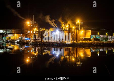 Papierfabrik in der Nacht. Winterfoto einer kleinen Fabrik mit Reflexion in einem See. Nachtszene in Bengtsfors, Schweden Stockfoto